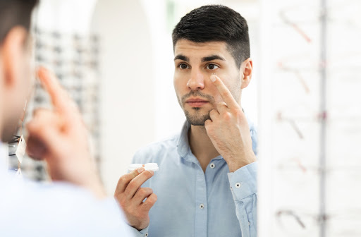 Man at the optometrist office putting on pair of contact lens in the mirror.
